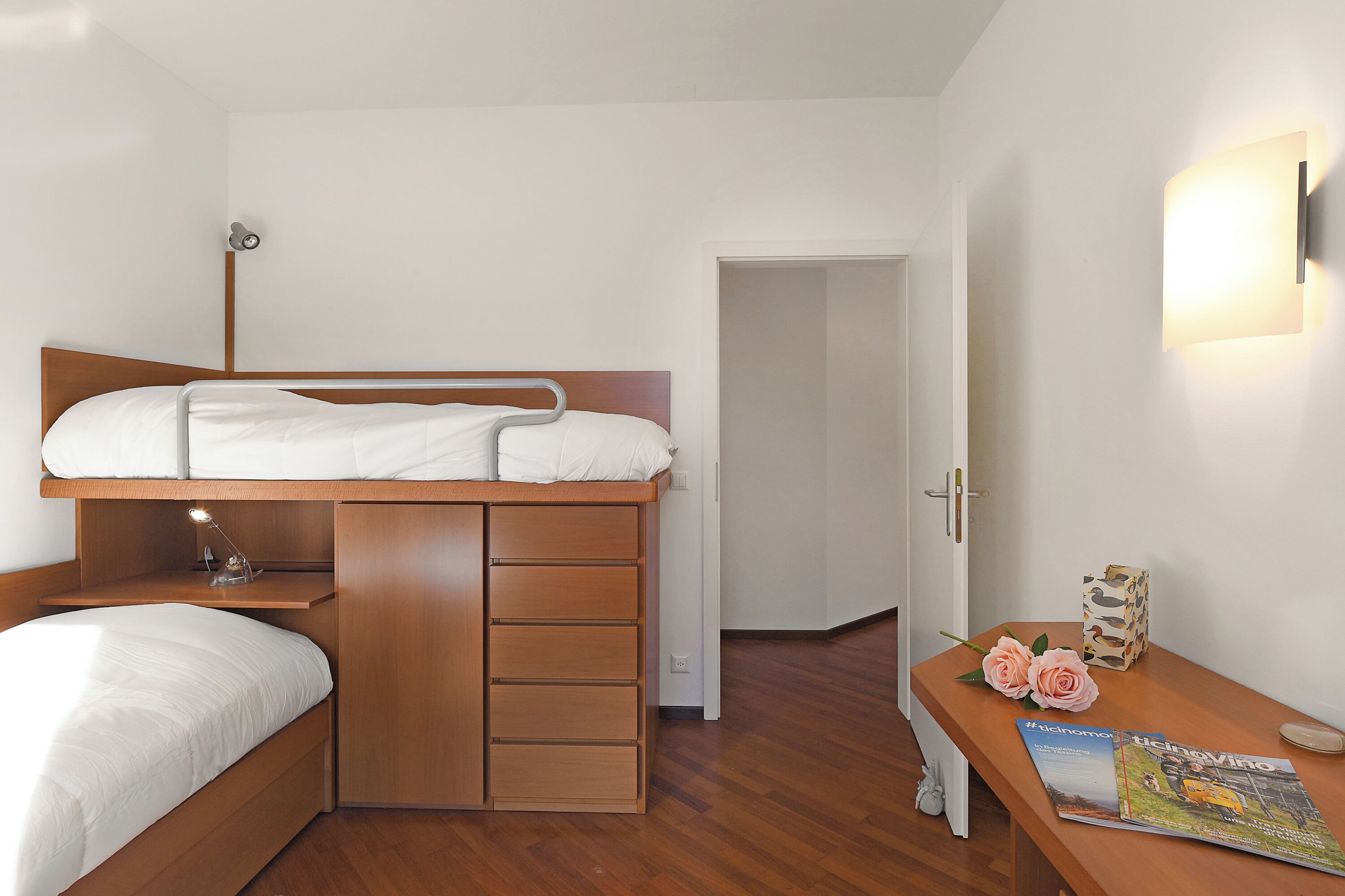Une chambre avec un lit superposé, un bureau avec une lampe, une chaise et un magazine posé sur le bureau.