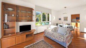 A living room with a TV, wooden entertainment unit, sofa, and dining area with a table and chairs. - Sweet Lake View Lugano (Lugano)