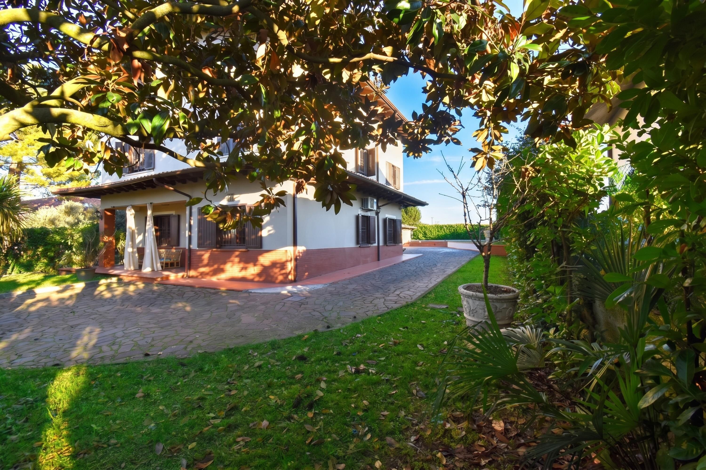 A house with a paved driveway, a garden with various plants, and a clear sky.