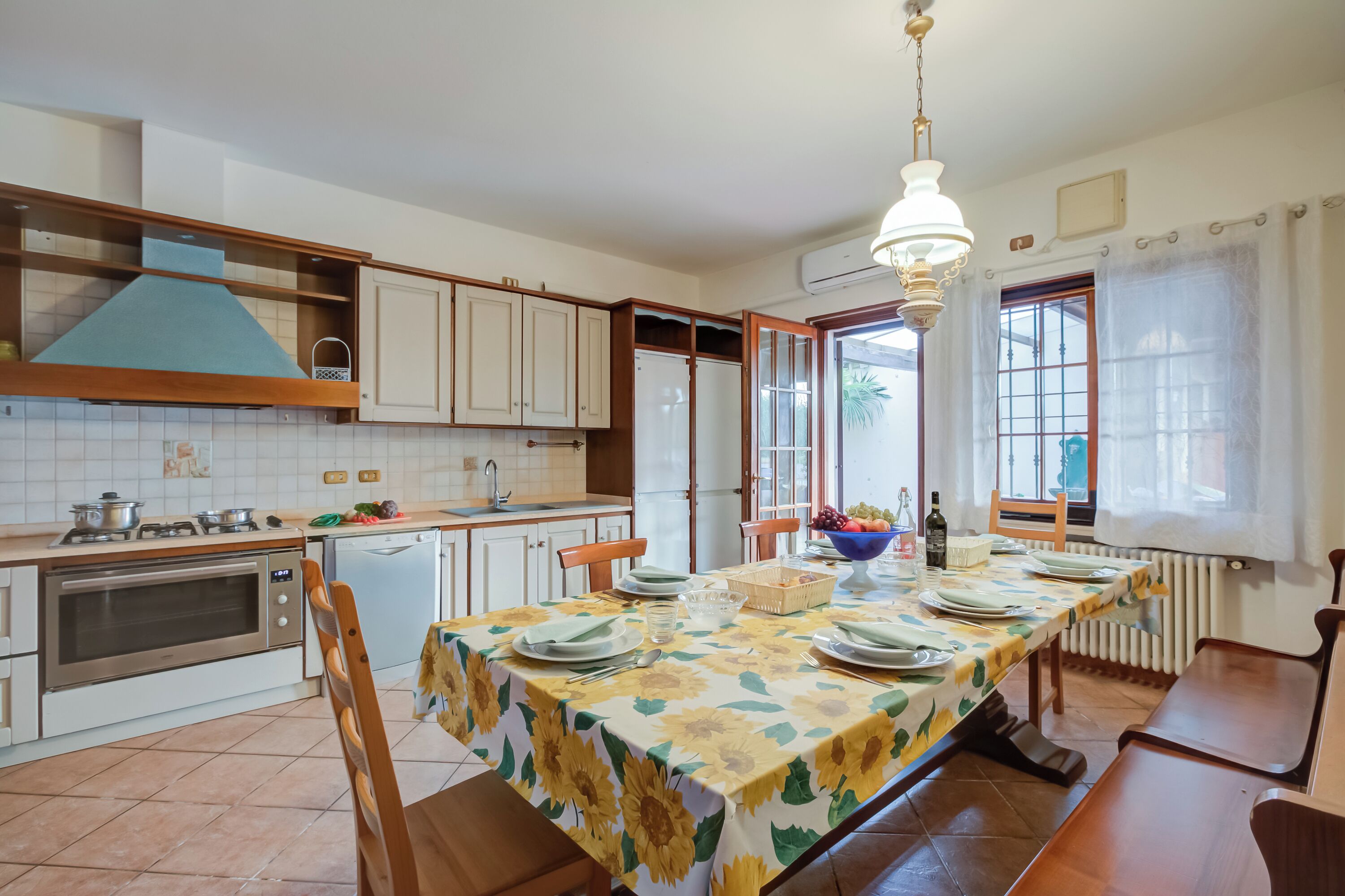 A kitchen with a dining table set for six, a built-in oven, and a window with curtains.