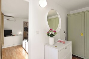 A bedroom with a white dresser, a mirror, a vase with flowers, a wardrobe, and a television in the background. - Apartment View And Pool (Agno)