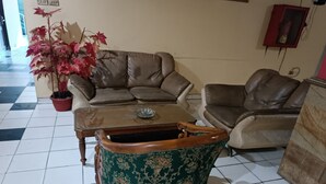 A living room with a brown leather sofa, a green patterned armchair, and a wooden coffee table with a glass bowl. - Hotel O Penginapan Laras PaminggirNearPesona Alam Seafood Pink Mira (Garut)