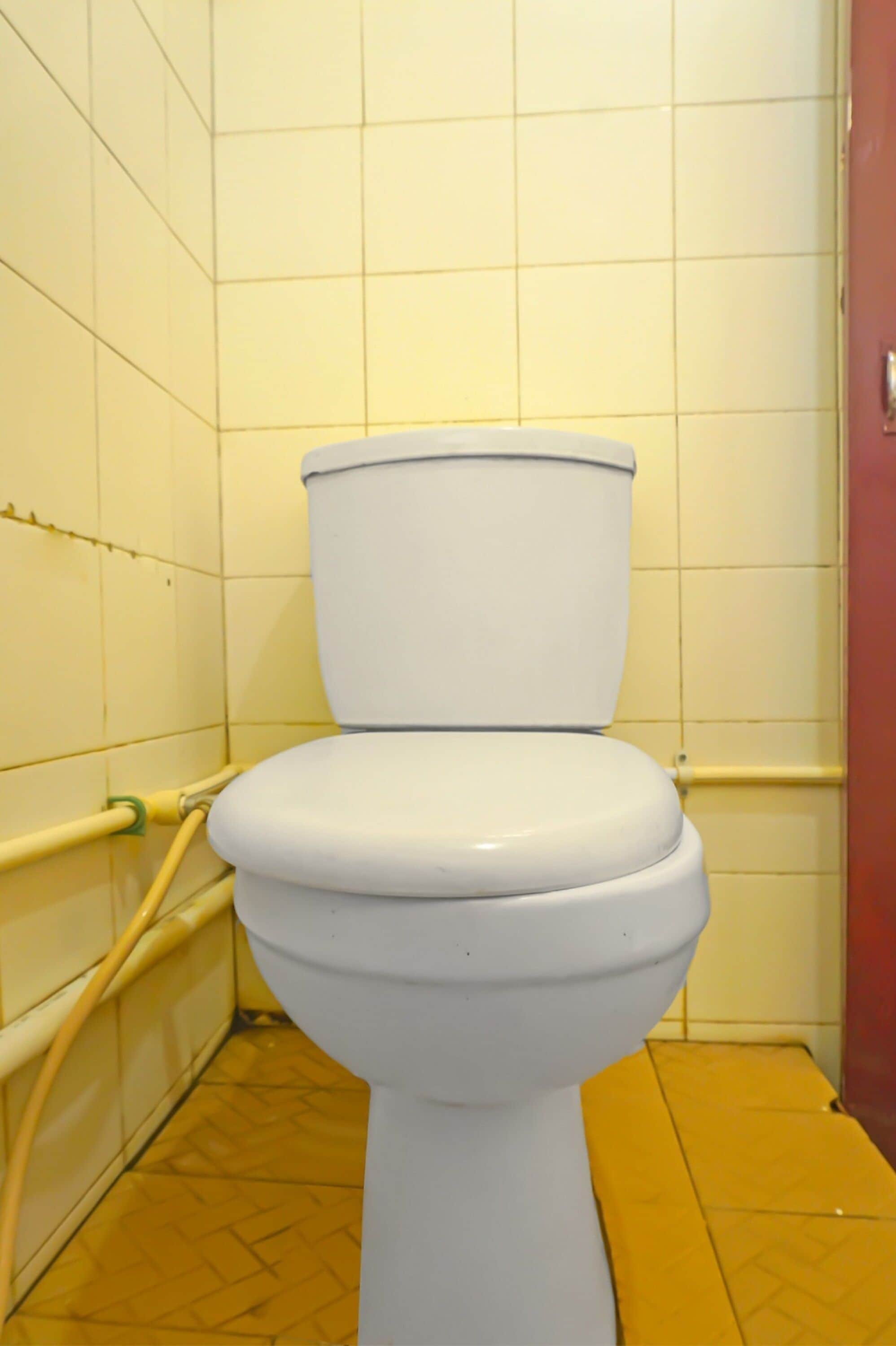 Un inodoro blanco en un baño con paredes y suelo de baldosas amarillas.