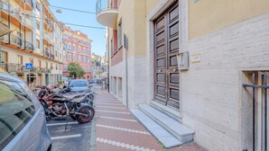 Une rue étroite bordée de motos et de voitures garées, des immeubles dotés de balcons et un chemin piétonnier.