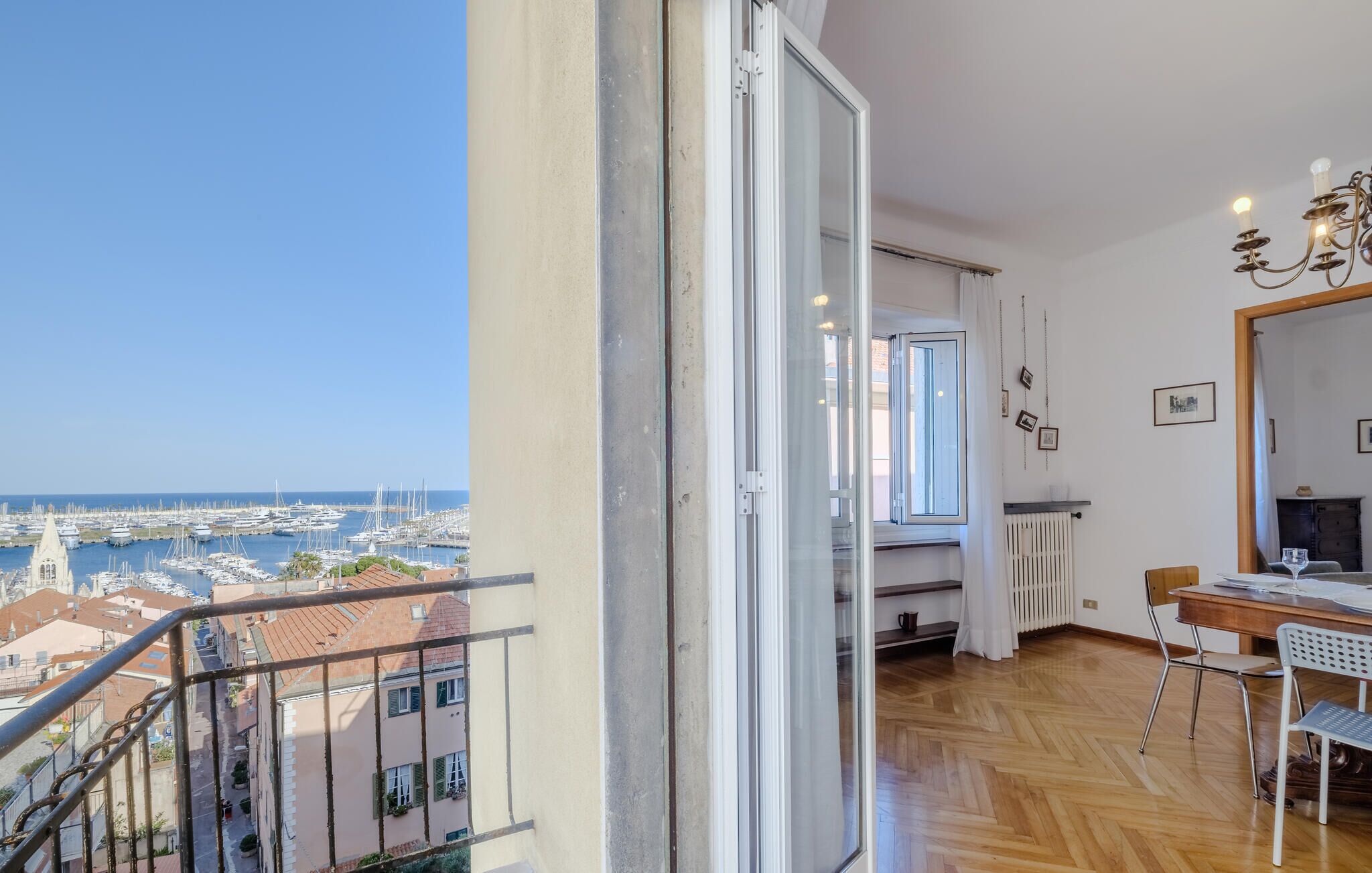 A balcony with a view of a marina and buildings, a dining area with a table and chairs, and a radiator on the wall.