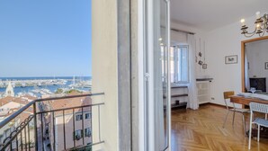 Un balcon donnant sur un port de plaisance et des immeubles, un coin repas avec une table et des chaises, et un radiateur fixé au mur.