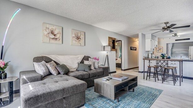 A modern living room with a grey sectional sofa, a coffee table, and a kitchen area with a bar stool. - Appaloosa - Unit A (Colorado Springs)