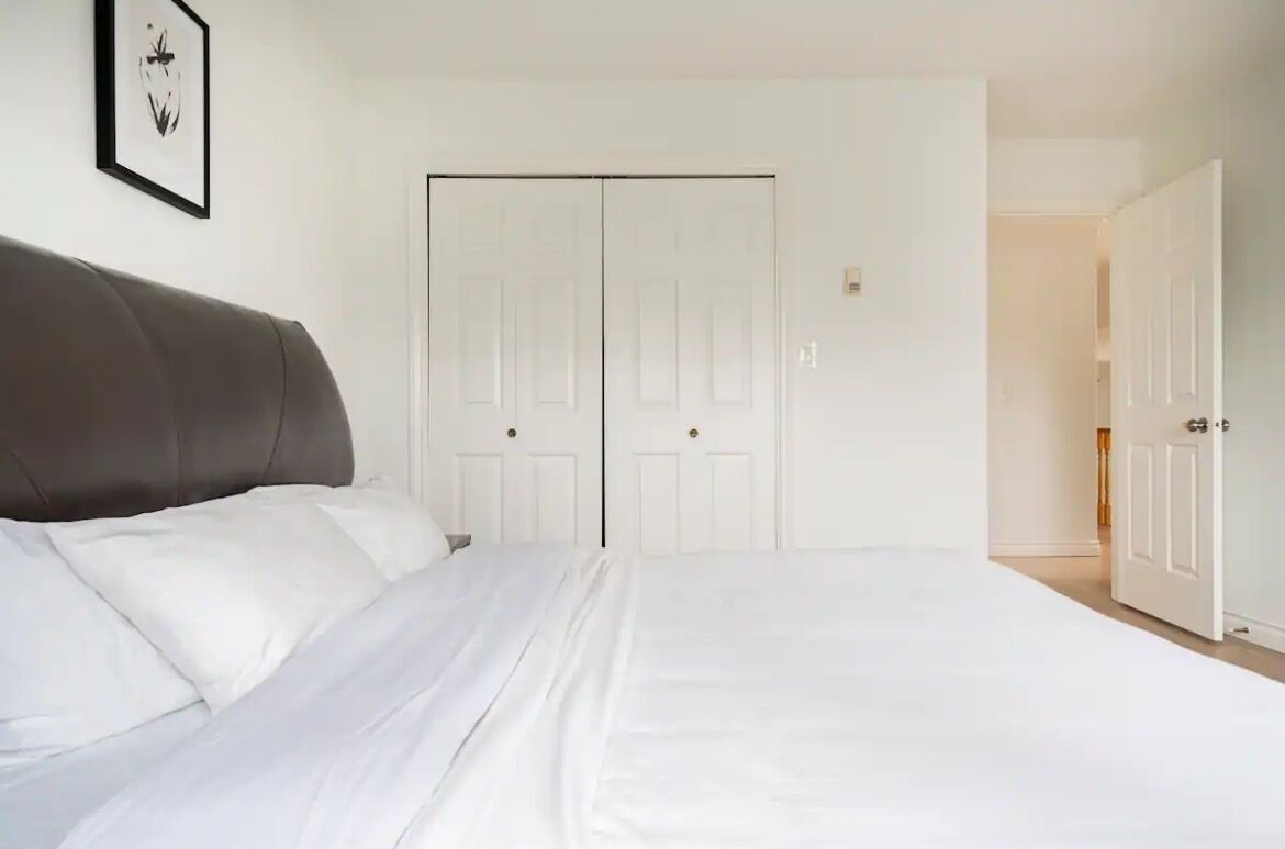A bedroom with a large bed, white bedding, a dark headboard, and a white wardrobe with double doors.