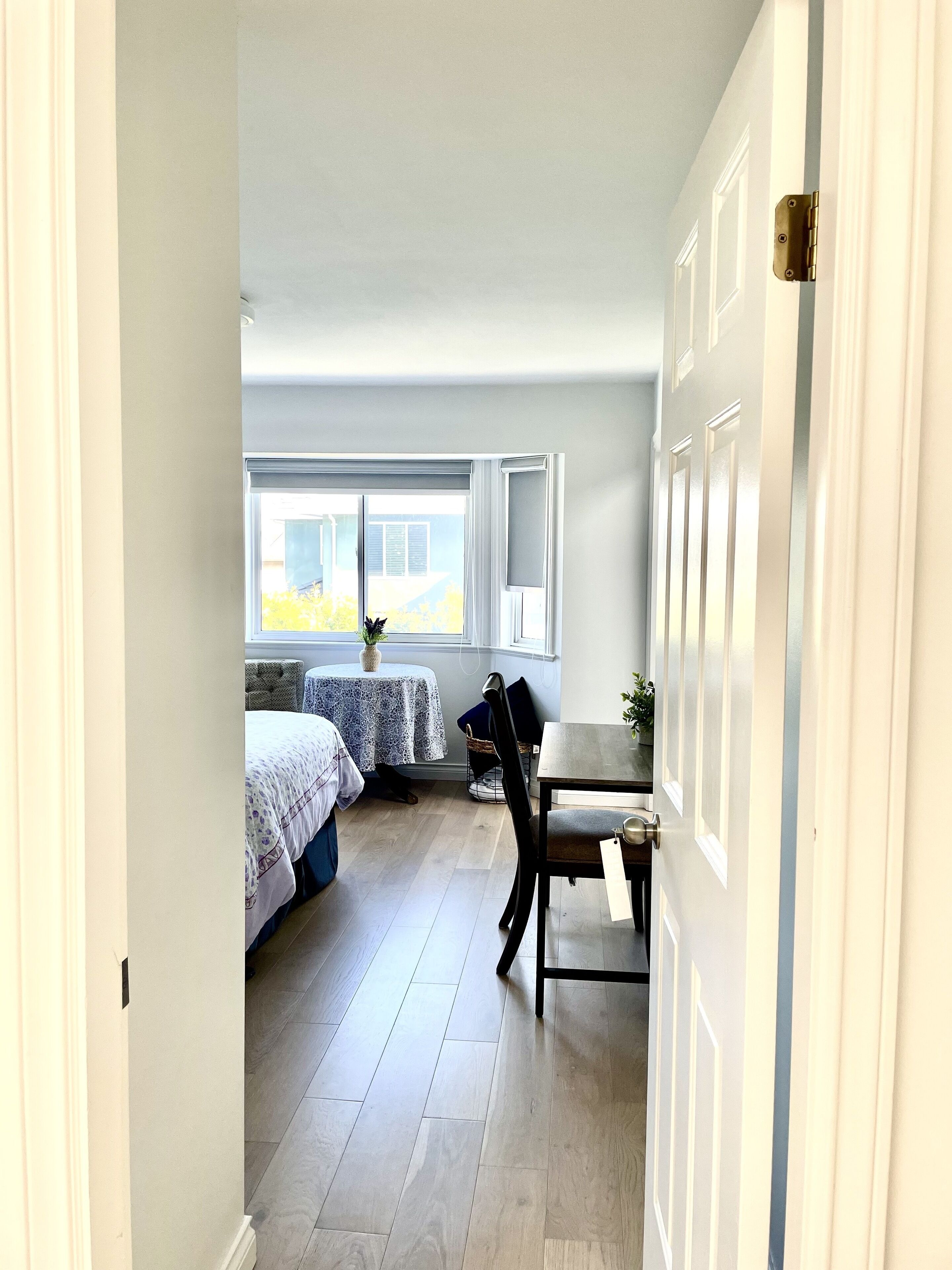 A narrow hallway leading to a bedroom with a bed, a table, and a chair.