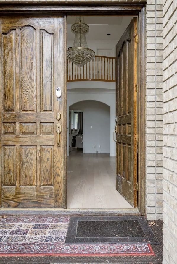 Une porte à deux battants en bois, avec un paillasson devant et un lustre au-dessus.