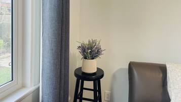 A room with a window, a grey curtain, a small stool with a plant, and a brown chair.
