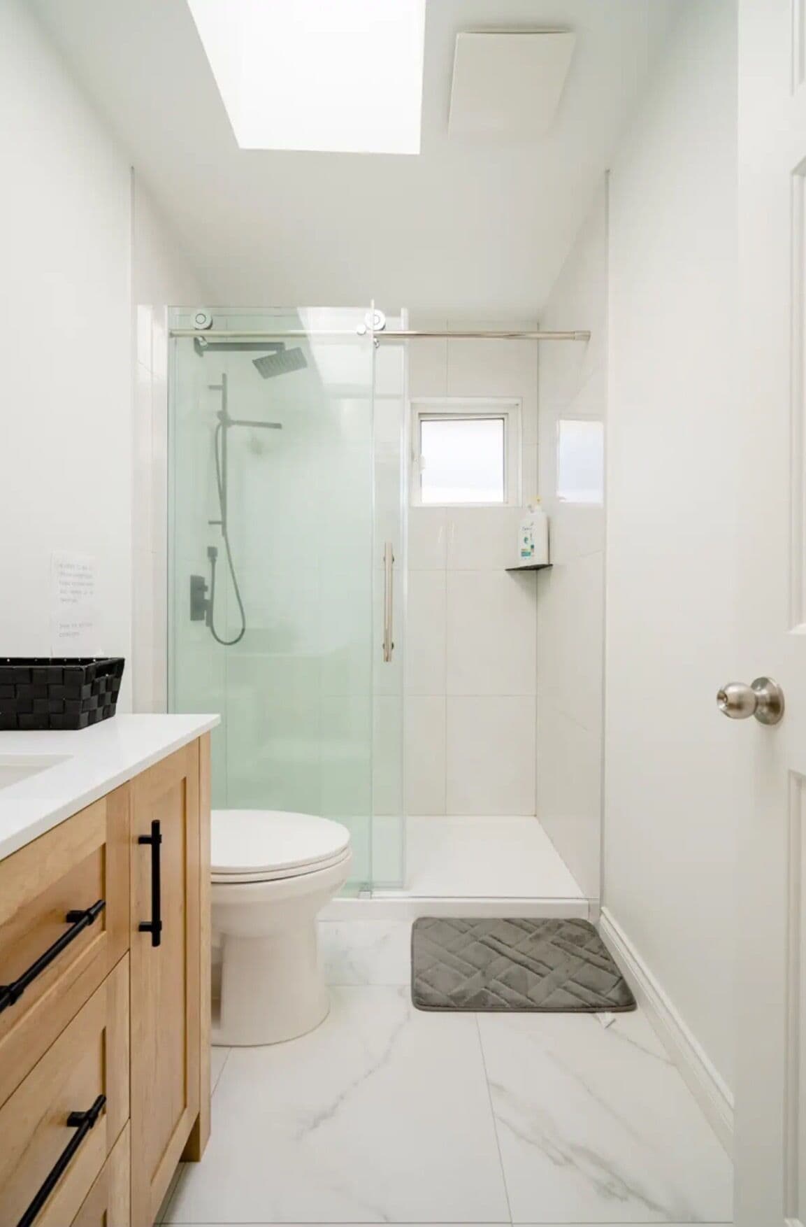 Un baño moderno con ducha de vidrio, inodoro y tocador con armarios de madera.