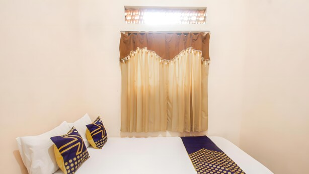 A hotel room with a bed, two pillows, a blanket, and a window with curtains. - Hotel O Bagas Homestay Near DWH (Tourism Village Green) BILEBANTE (Mataram)