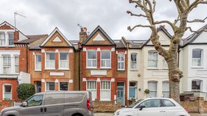A row of terraced houses with a grey van and a white car parked on the street.