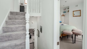 A staircase with patterned carpet leading to a bedroom with a bed, a bedside table, and a hanging light fixture.
