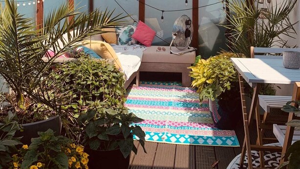 A cozy outdoor seating area with a cushioned bench, a table, and a large umbrella providing shade.