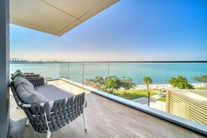 A balcony with a view of the sea, a seating area with cushions, and a clear sky.
