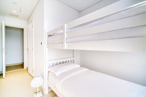 Ein Schlafraum mit Etagenbetten, weißer Bettwäsche und einer weißen Lampe.