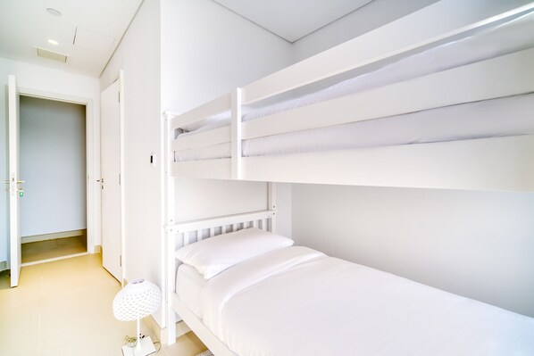 A bunk bed room with white bedding and a white lamp.