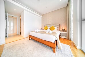 A bedroom with a large bed, a bedside table with a lamp, and a door leading to another room.