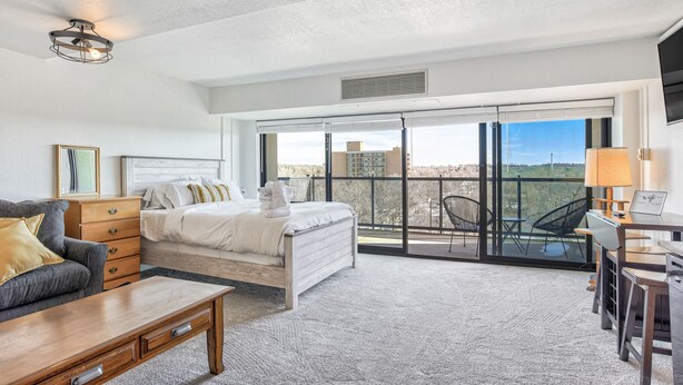 A modern hotel room with a large bed, a sofa, a desk, and a balcony with a view. - Mid-Nest Unit 708 (Colorado Springs)
