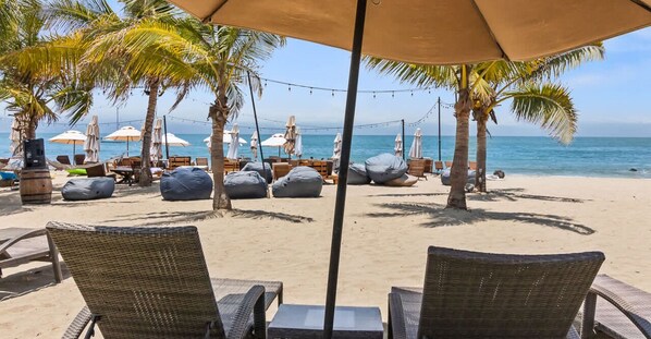 A beachside lounge with wicker chairs, bean bags, and umbrellas.