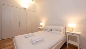 Een slaapkamer met een groot bed, twee nachtkastjes met lampen, een kledingkast en een houten vloer.