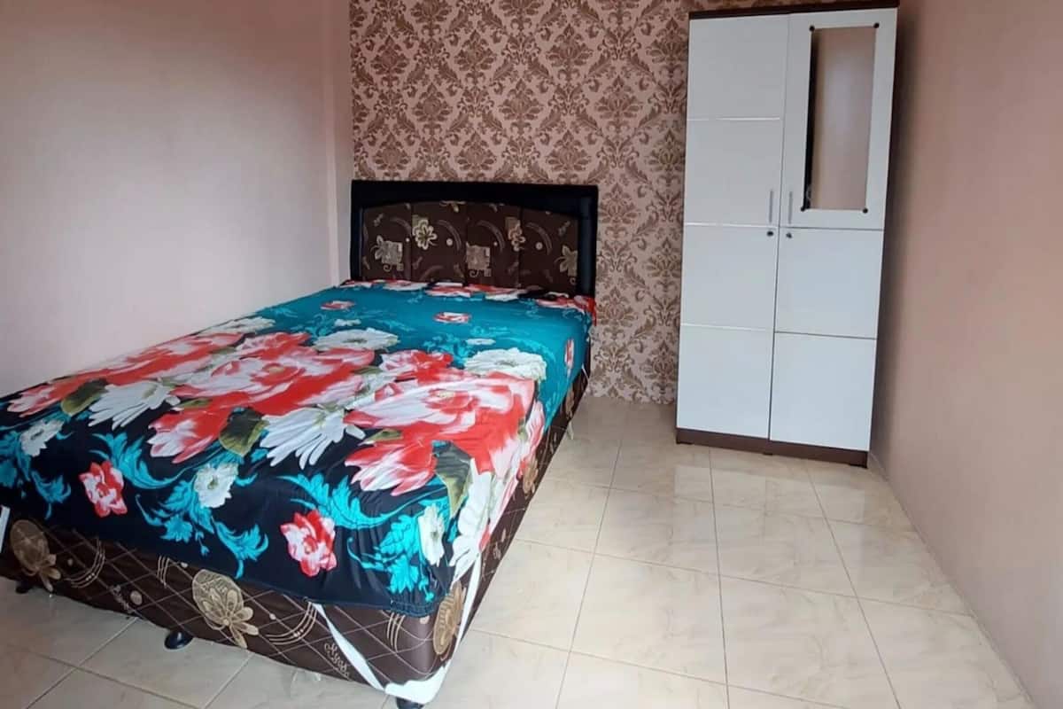 A bedroom with a bed, a wardrobe, and patterned wallpaper.