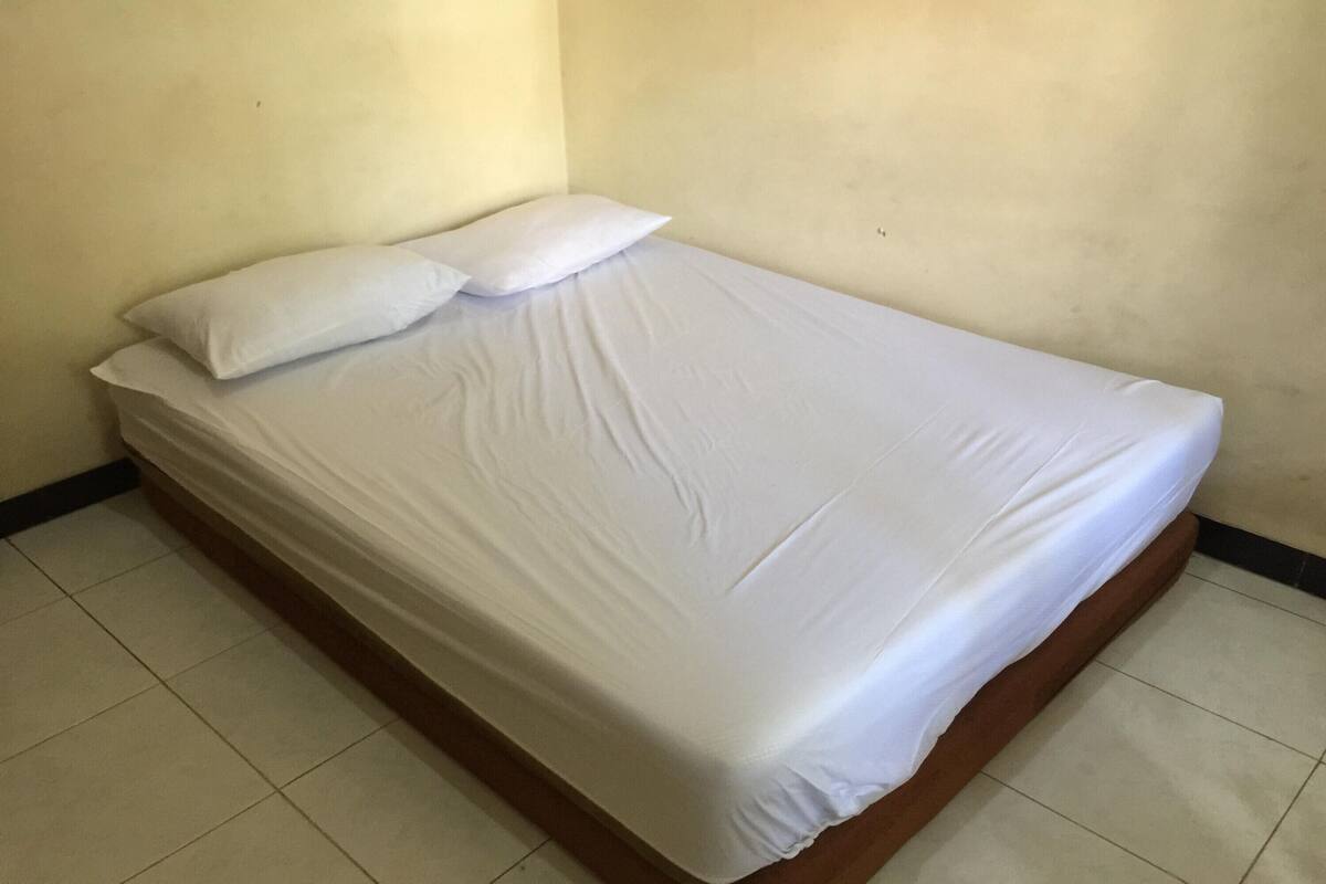 A single bed with white bedding in a room with plain walls and tiled flooring.