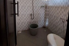 Bathroom with toilet, shower, and trash bin.
