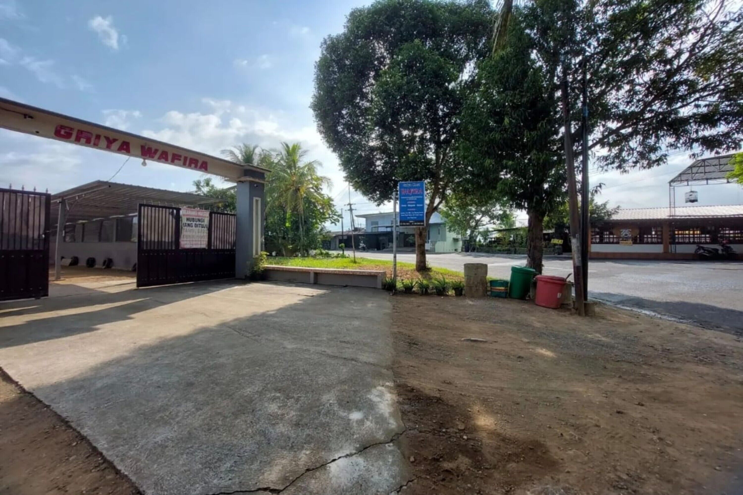 A gated entrance with a sign reading "GRIYA WAFIRA" and a blue signboard in the background.