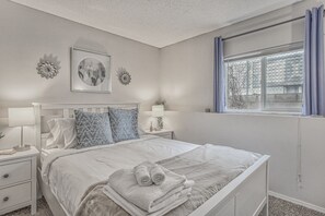 Cozy retreat with a neatly made bed, nightstand, and window with a view.