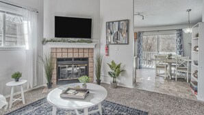 A modern living room with a fireplace, a flat-screen TV, and a dining area with a table and chairs. - Mid-GoodnightVenture (Colorado Springs)