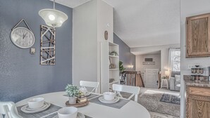 A modern dining area with a round table, white chairs, and a chandelier. - Mid-GoodnightVenture (Colorado Springs)