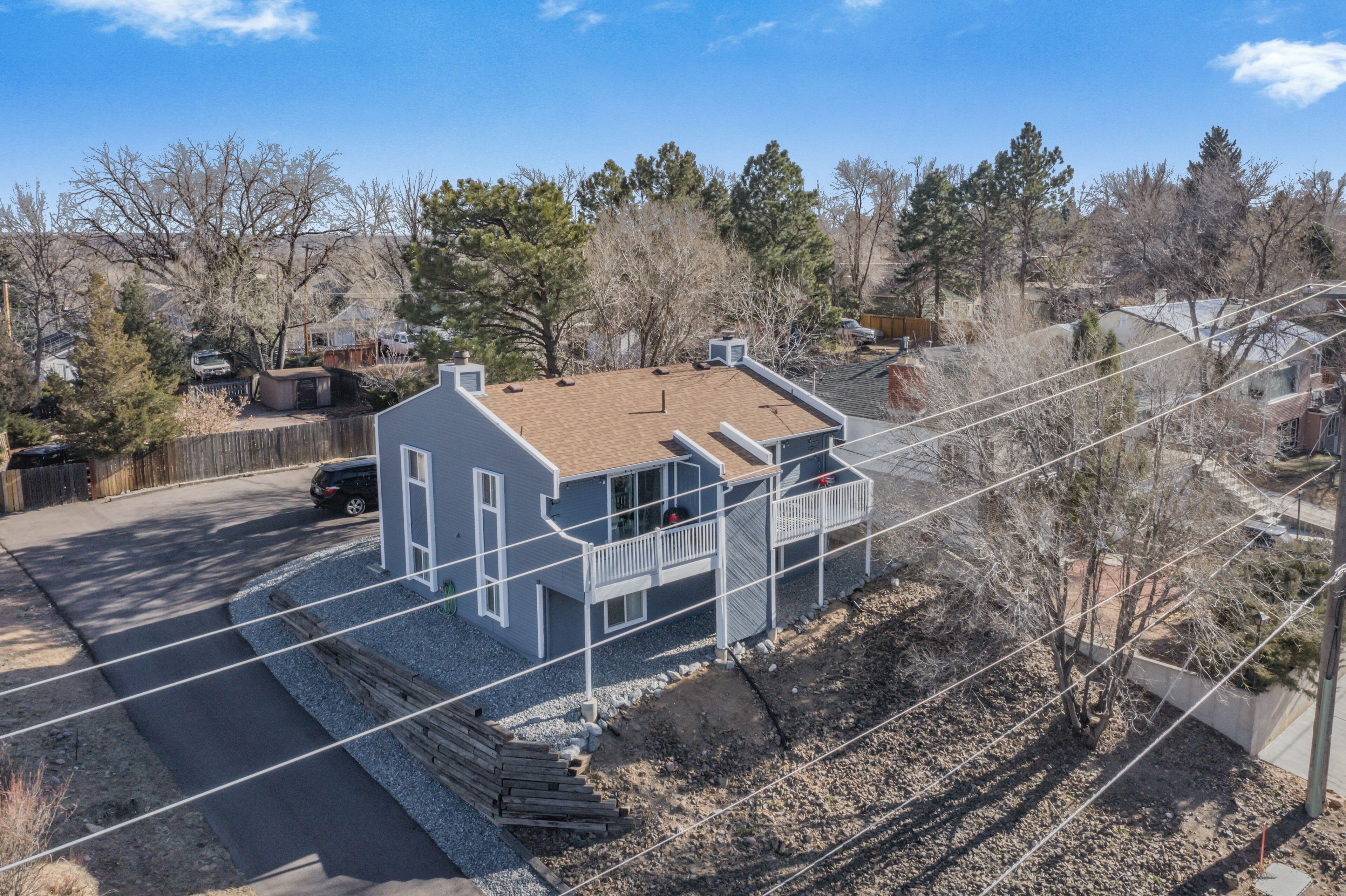 A two-story house with a sloped roof, a fenced yard, and a clear sky.