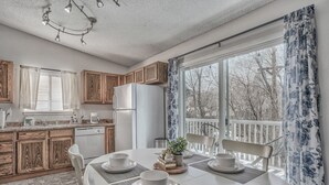 A modern kitchen with wooden cabinets, a white refrigerator, and a dining table set for four. - Mid-GoodnightVenture (Colorado Springs)