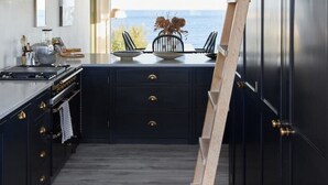 A modern kitchen with dark cabinetry, a wooden ladder, and pendant lighting. - Stunning architect designed eco beachfront property (Selsey)