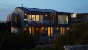 A modern two-story house with a balcony, large windows, and a stone facade. - Stunning architect designed eco beachfront property (Selsey)