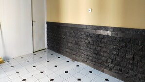 A hallway with a tiled floor, a white door, and a wall with a stone accent. - Hotel O Guest House Zidan 21 (Tanahgrogot)