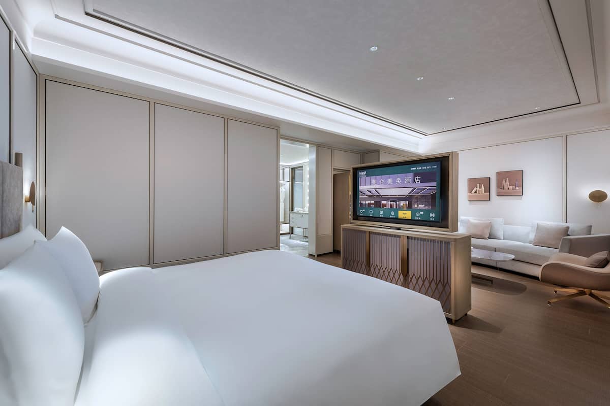 Una habitación de hotel moderna con una cama grande, un televisor, un sofá y un diseño minimalista.
