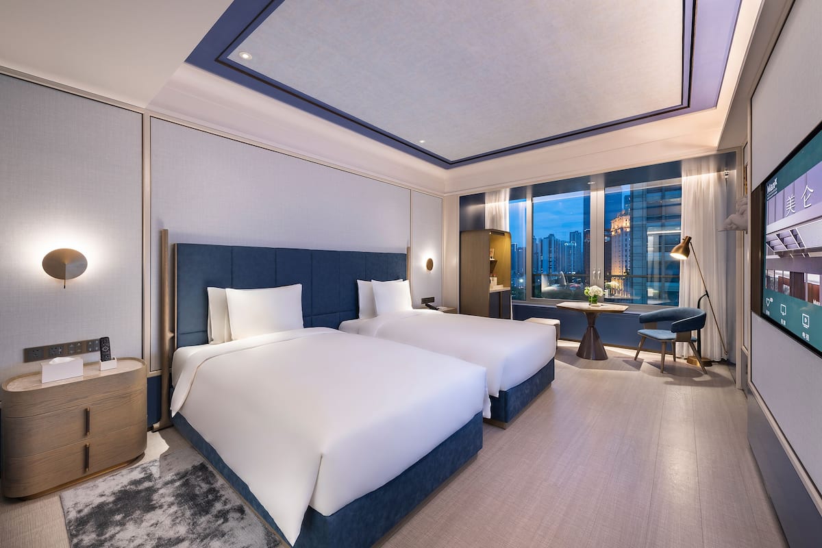 Habitación de hotel moderna con dos camas, un escritorio y un ventanal con vistas a la ciudad.
