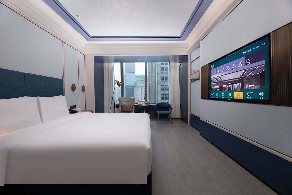 Habitación de hotel con una cama grande, un escritorio, una silla y un televisor mostrando información del hotel.