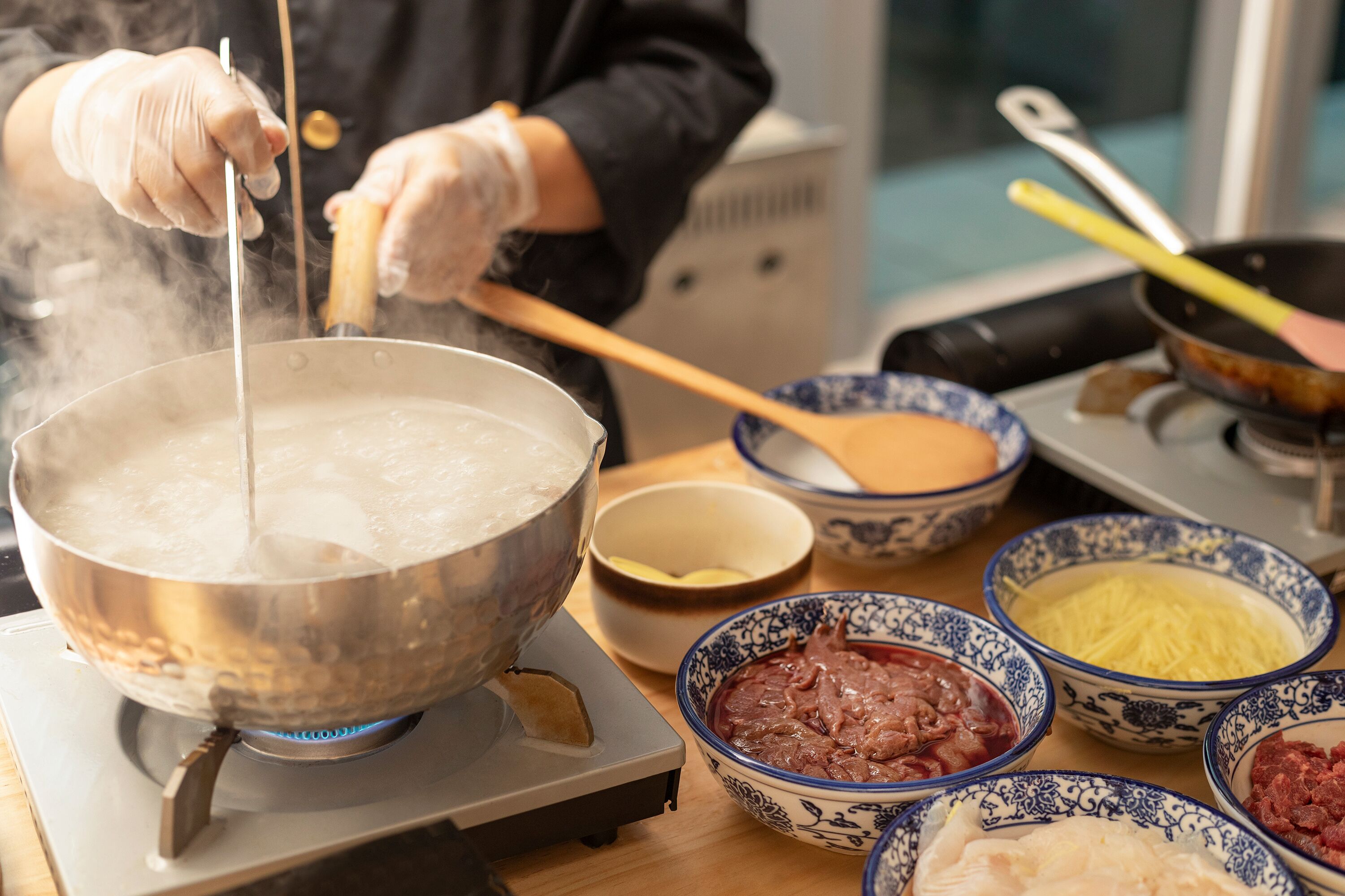 Una persona cocinando en una hornilla portátil, rodeada de tazones con diversos ingredientes.