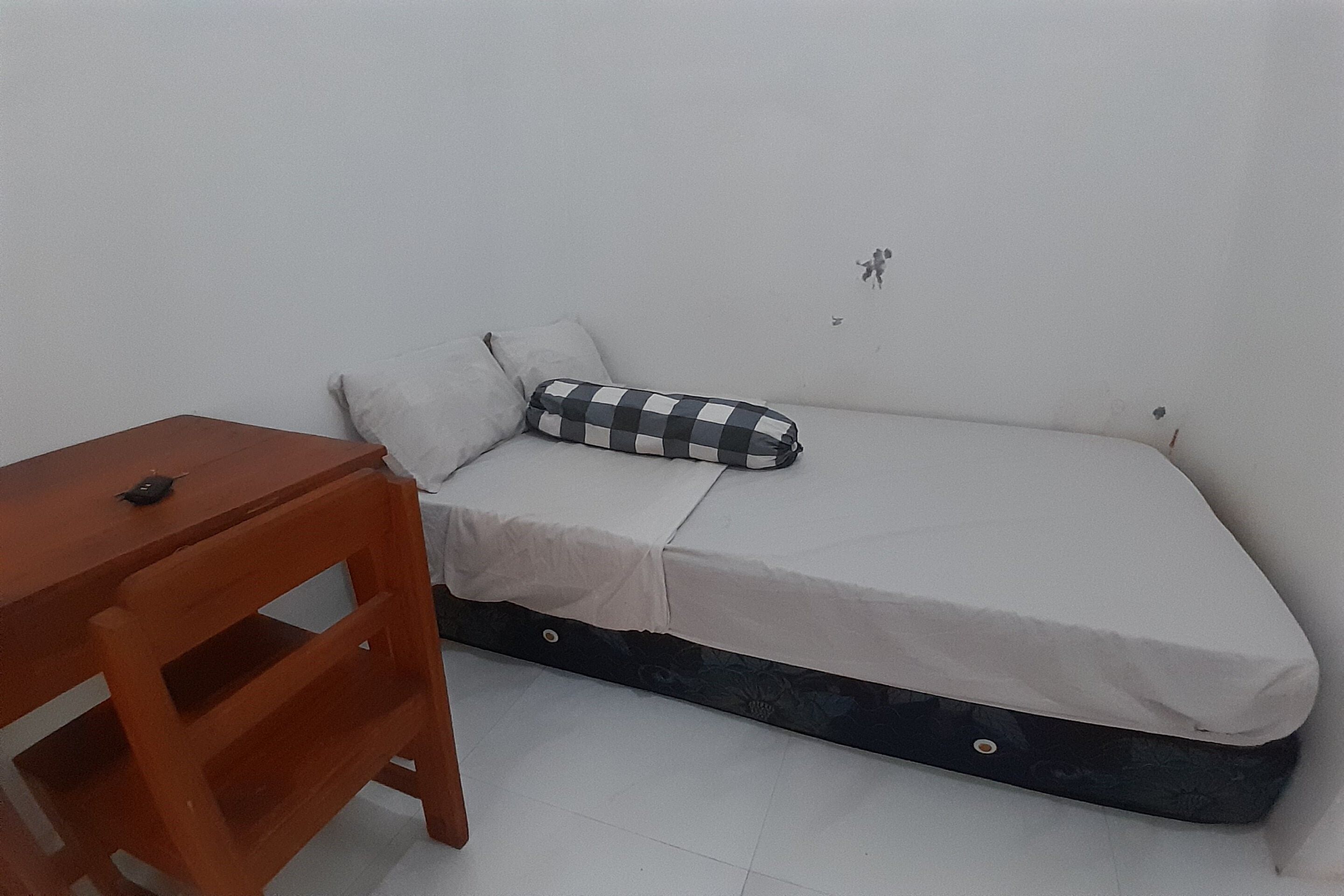 A single bed with a checkered pillow, a wooden nightstand, and a small table.