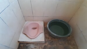 Une petite salle de bain avec des toilettes roses et un grand seau.