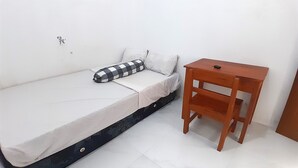 Un lit simple avec un oreiller à carreaux, une table de chevet en bois et un mur blanc.