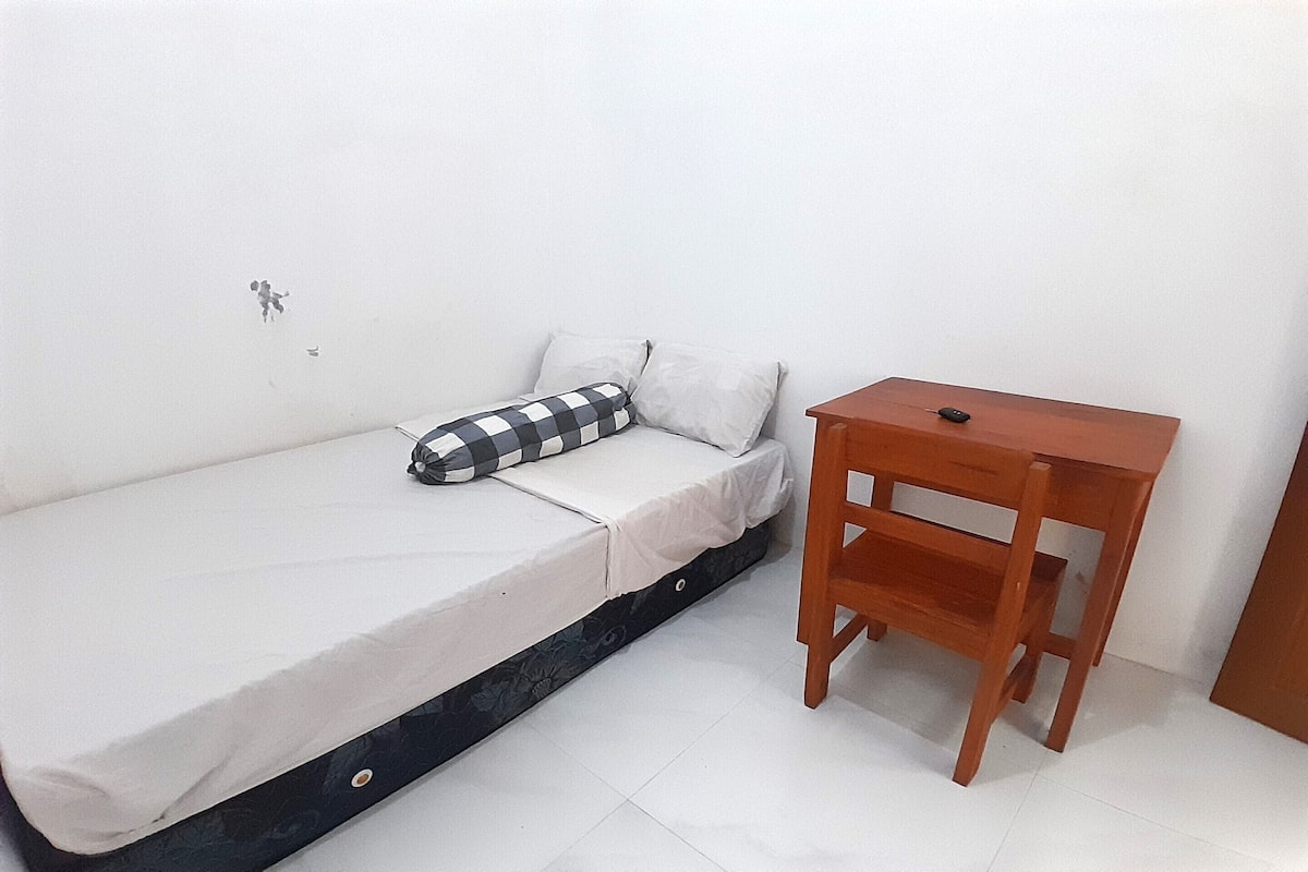 A single bed with a checkered pillow, a wooden nightstand, and a white wall.