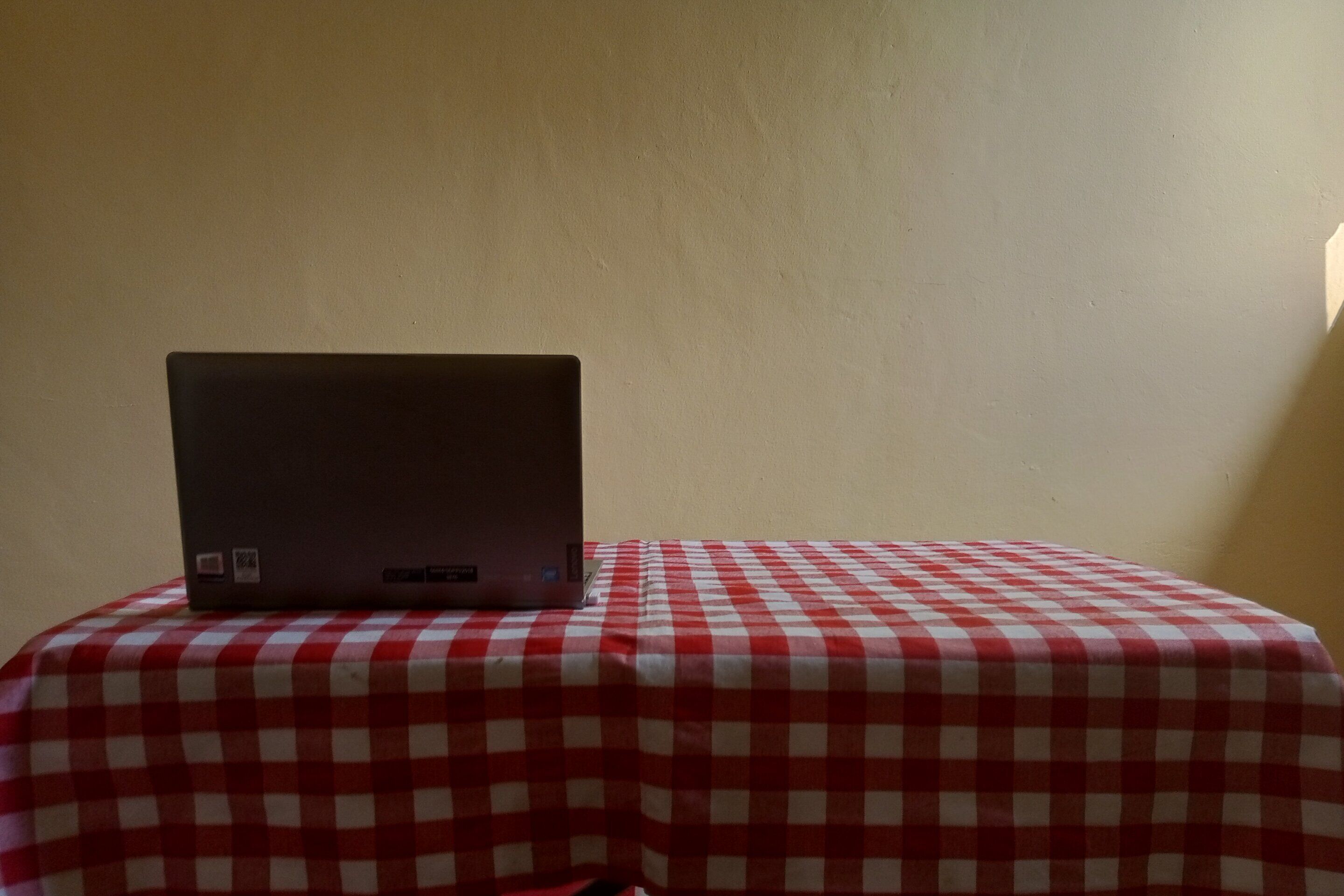 A laptop on a table with a red and white checkered tablecloth.