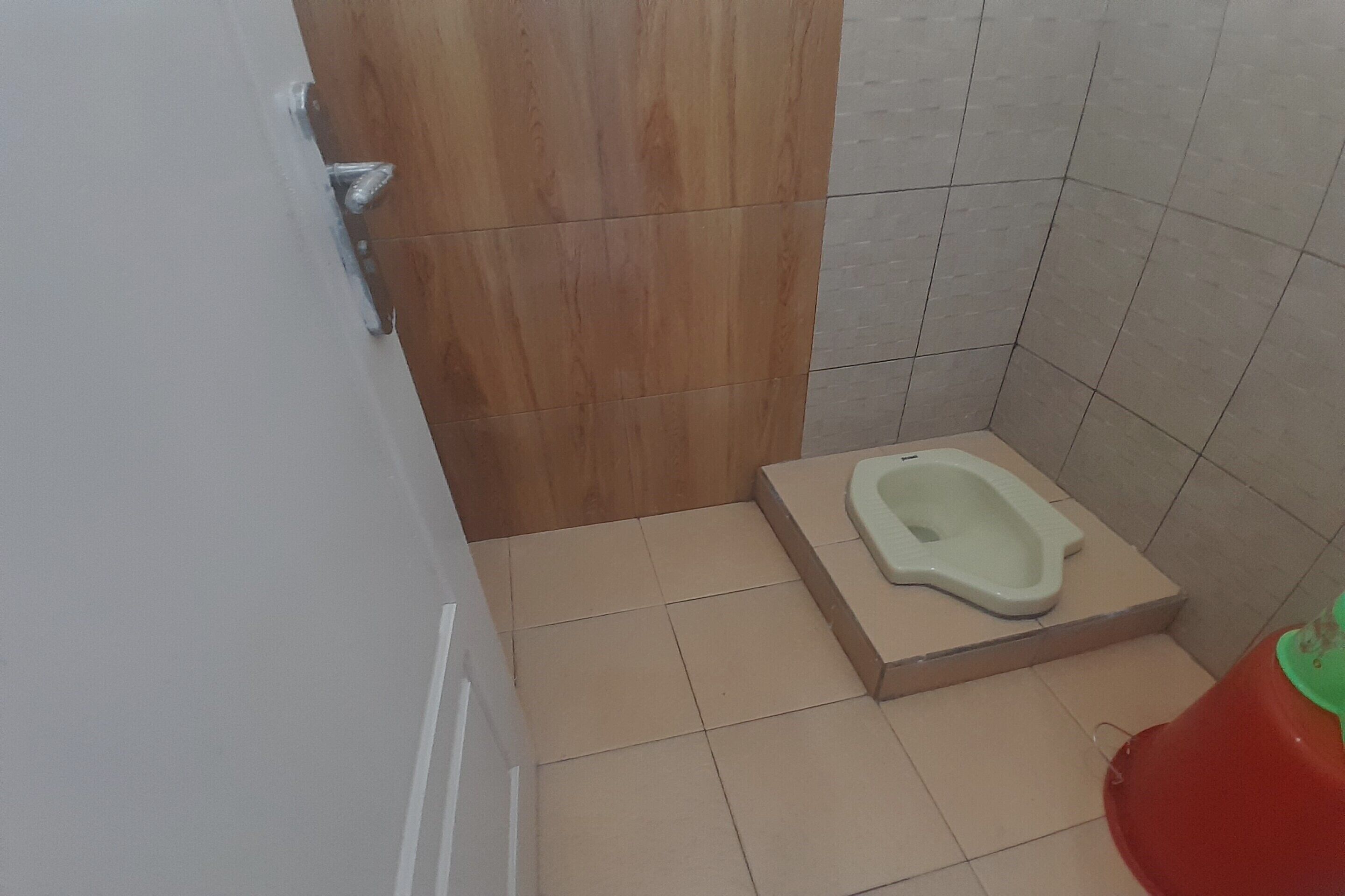 Un baño pequeño con un separador de madera, un inodoro blanco y un balde rojo.