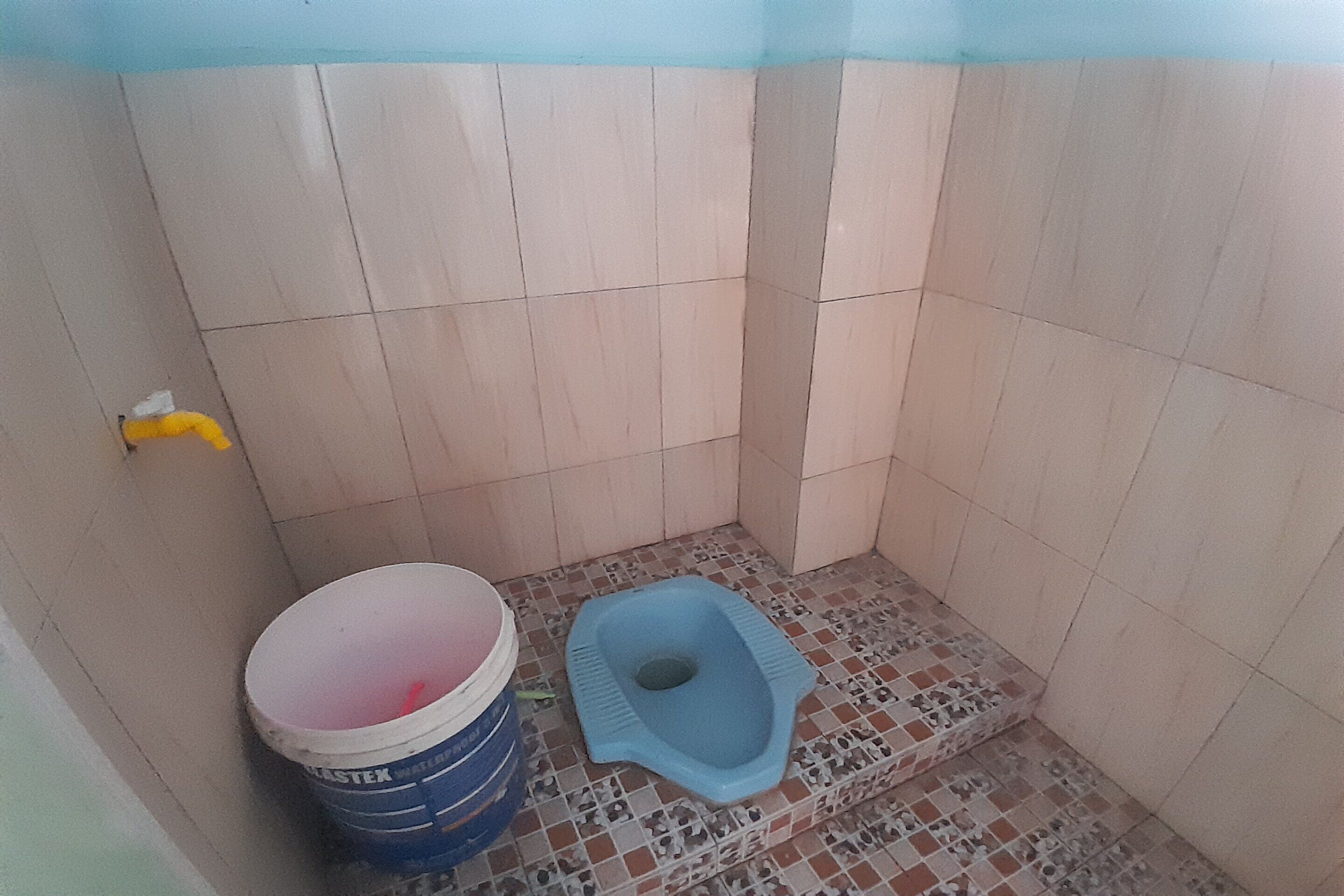 Un baño pequeño con inodoro azul, un cubo blanco y una barandilla amarilla.